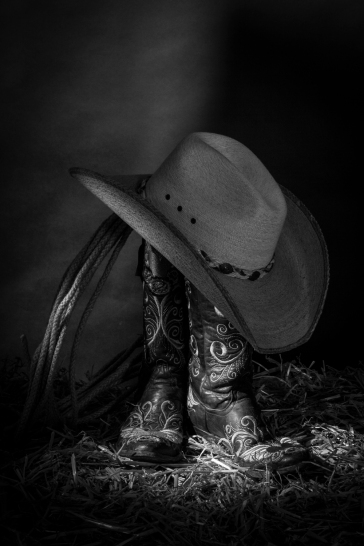 Black and white still life photograph of cowboy boots and hat